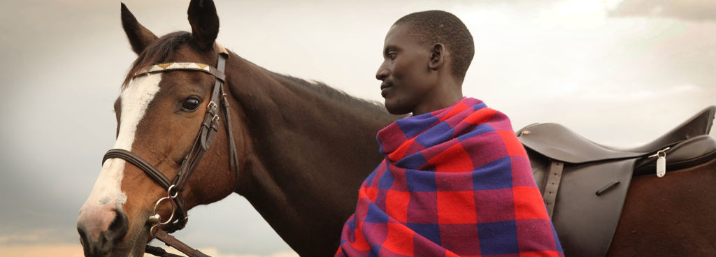 A Maasai tribesman stands with a horse on an African riding safari