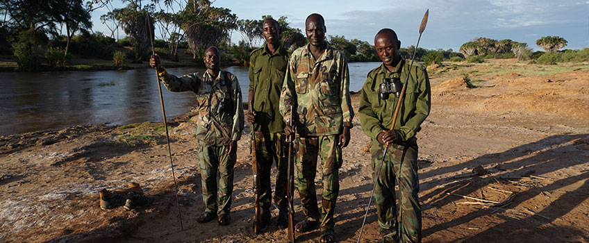 African walking safari guides and rangers pose on the bank of a river