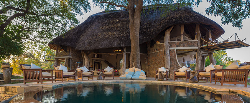 A view across a swimming pool to the main thatched lodge at Luangwa Safari House.