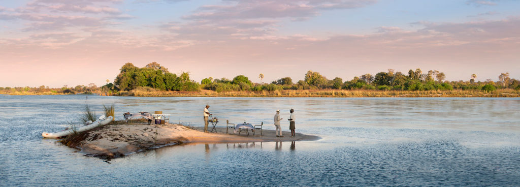 Private island sundowner setup on the river with drinks, chairs, and a guide preparing refreshments.