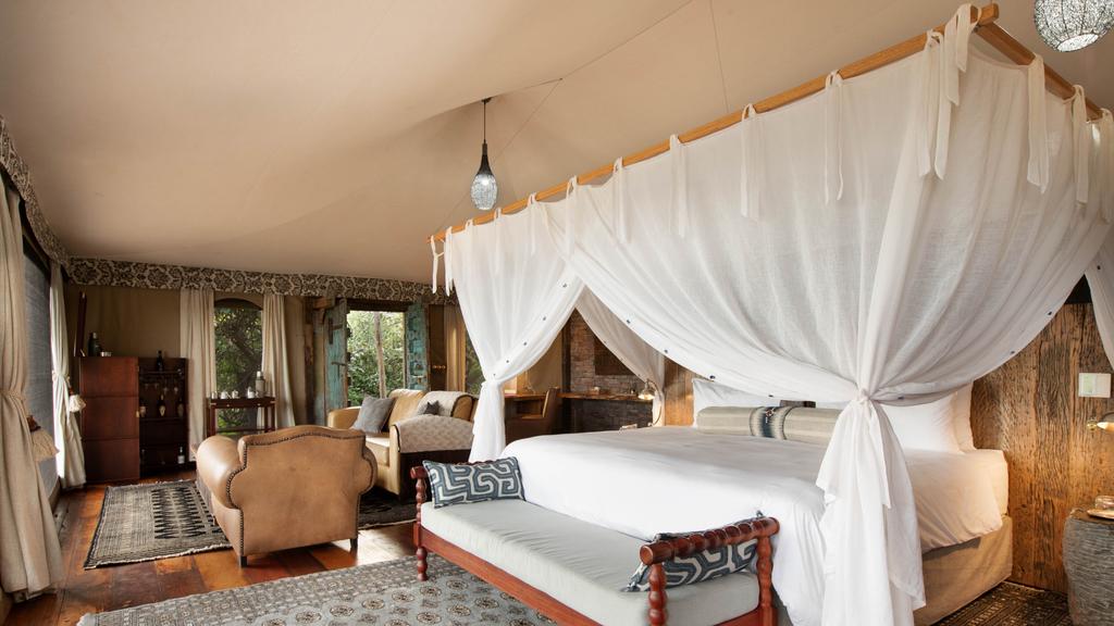 uxury safari tent suite at Tembo Plains Camp in Sapi Reserve, Zimbabwe, showcasing a king-size bed with mosquito netting, elegant safari-style furniture, and natural wood finishes.