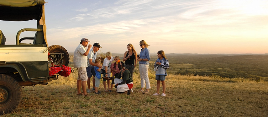 Family gathers with local guide at sundown on a grassy ridge overlooking Kenya’s Loisaba Conservancy.