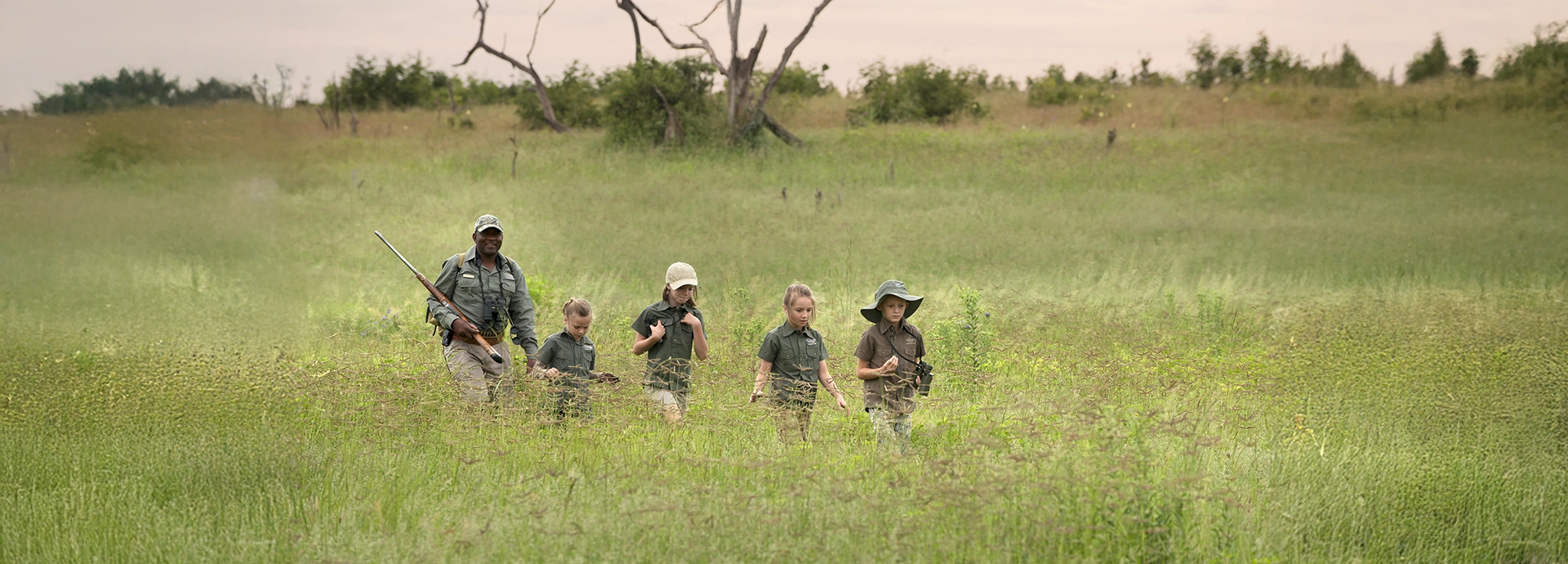 Young adventurers in safari gear explore the grasslands on foot with their guide at Somalisa Acacia.