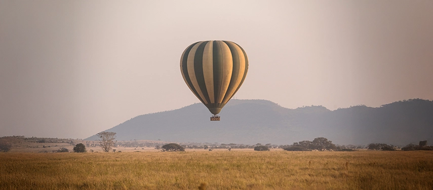 Hot air balloon floating above the Serengeti plains with distant hills in the background.