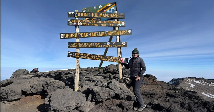 Melanie Hochkins from The Classic Safari Company standing at Uhuru Peak sign, the 5895m summit of Mount Kilimanjaro, Tanzania.
