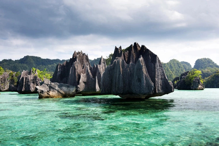 Dramatic limestone karsts rising from emerald waters in Raja Ampat’s pristine Indonesian archipelago.