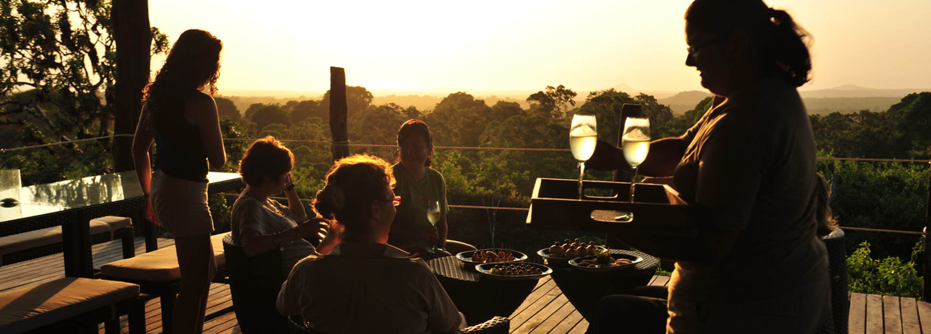 A group of tourists enjoy sundowners at Galápagos Safari Camp with expansive views of the highland forests
