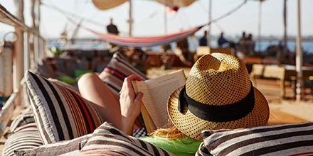 A relaxed traveller reads in the shade on deck, surrounded by colourful cushions and the gentle rhythm of the river.