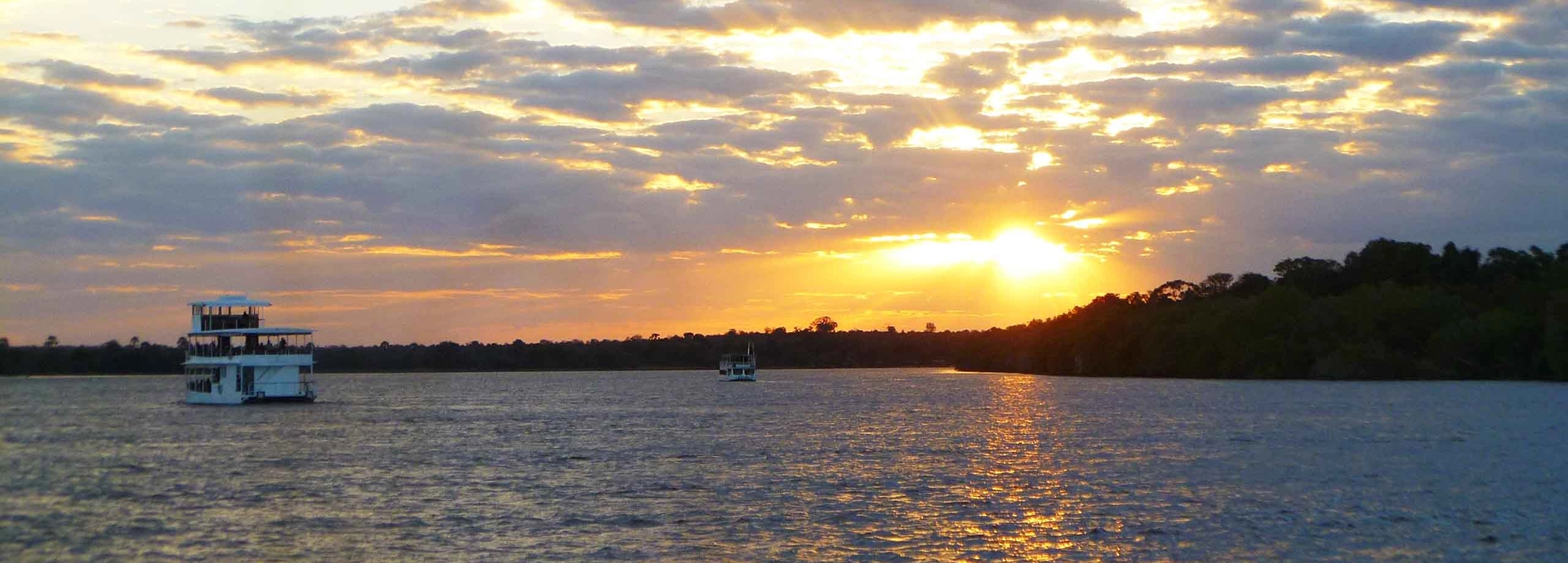 Sunset cruise on the Zambezi River with boats silhouetted against the glowing sky on the Grand Zambezi Safari.