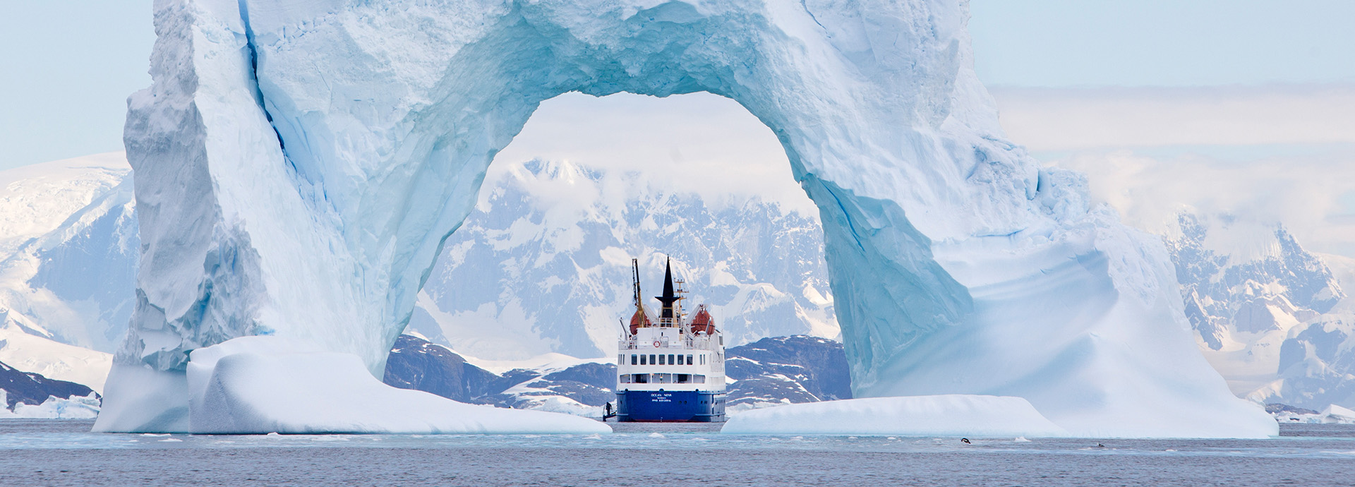 Ship cruises through an archway in an immense iceberg in Antarctica