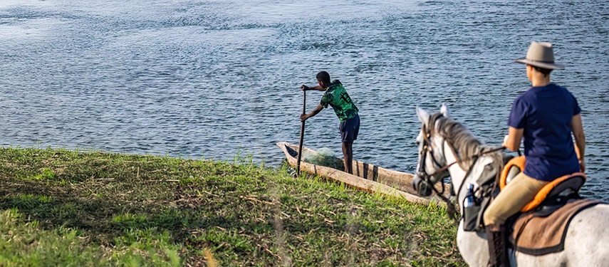 Horseback rider observing a fisherman paddling a mokoro along the banks of the Zambezi River.