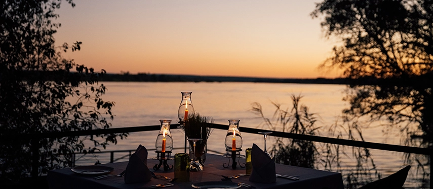 Lantern-lit dinner overlooking the Zambezi River at sunset from Chundukwa River Lodge.