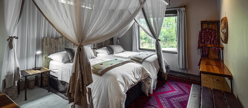 Canopied twin bedroom with mosquito nets and natural timber furnishings at Chundukwa River Lodge.