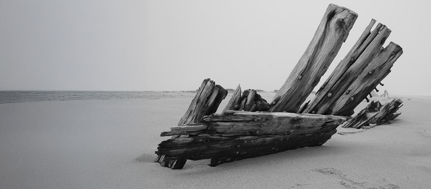 Black and white phot of the skeletal remains of a wooden ship, half-buried in sand on Namibia's Skeleton Coast