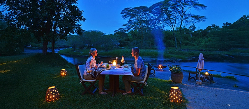 Candlelit riverside dining under twilight sky at Ishasha Wilderness Camp