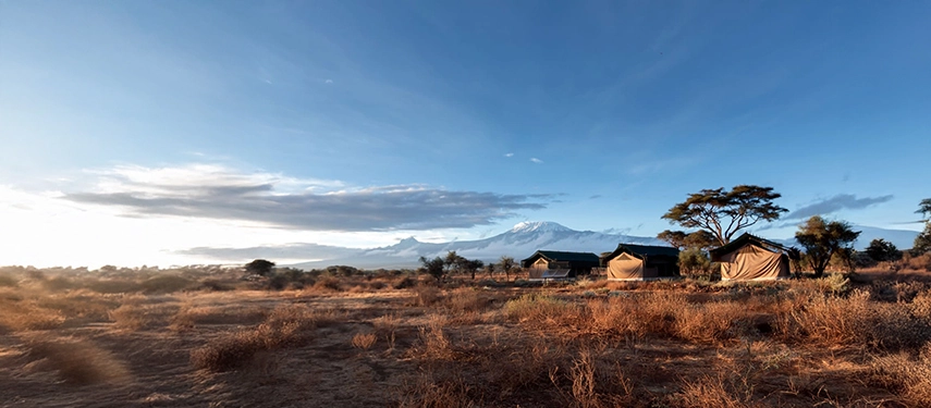 Scenic safari camp in Tanzania with classic tents set against the dramatic backdrop of Mount Kilimanjaro at sunrise.