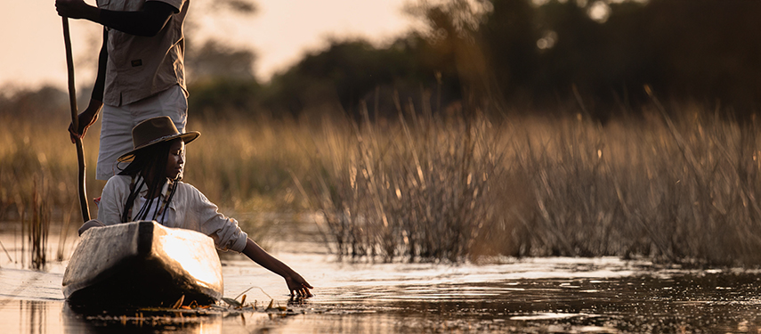 Guest trails her hand in the water during a sunset mokoro journey.