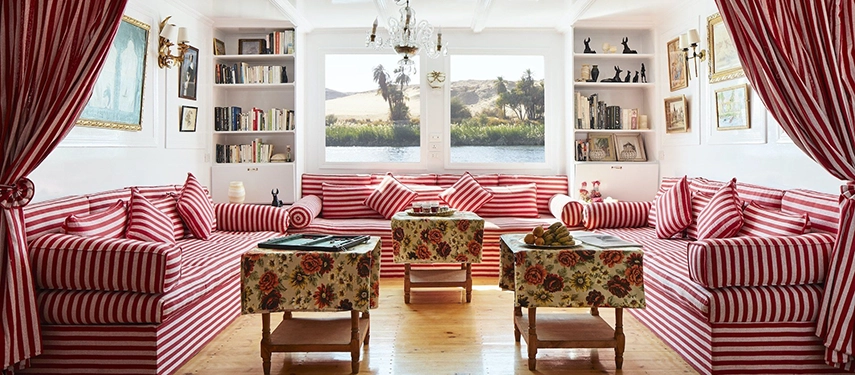A cosy dahabiya salon with striped sofas and river views creates a warm & inviting retreat as the Nile drifts by.