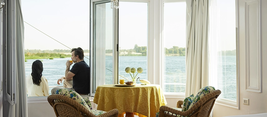 A couple sits by wide open windows, enjoying breakfast with uninterrupted views of the Nile drifting past.