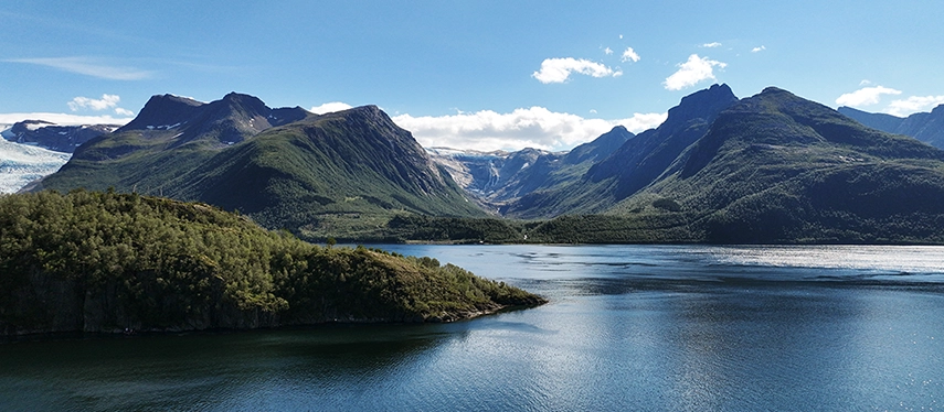A tranquil Norwegian fjord framed by green mountains under a bright blue sky.