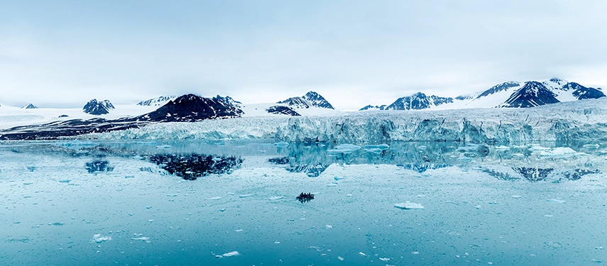 A Zodiac tender gliding across turquoise Arctic waters below distant glaciers.
