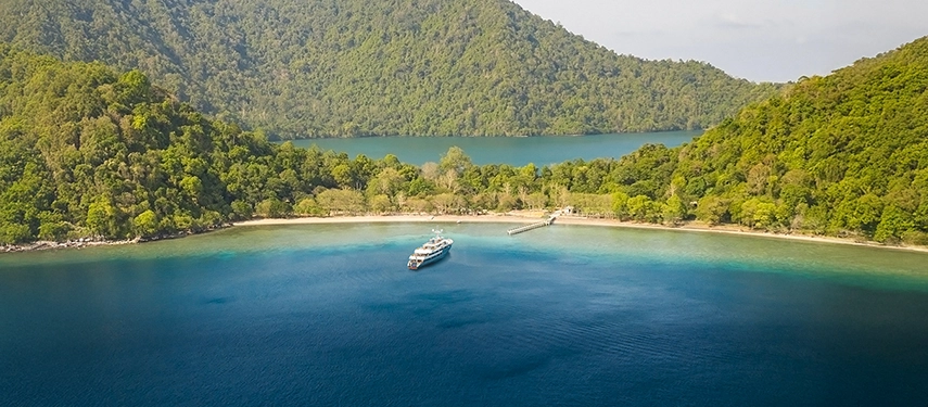 Aqua Blu resting in a secluded cove fringed by emerald forest and turquoise shallows, the embodiment of remote luxury.