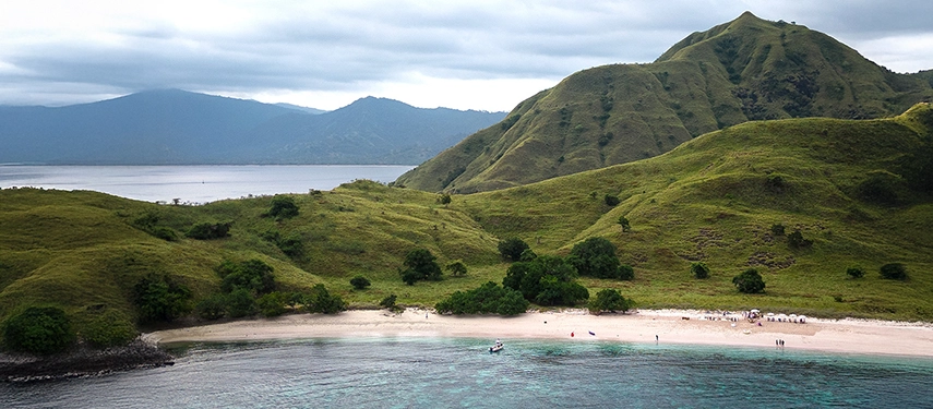 Aqua Blu anchored offshore as guests wade in the shallows near a sunlit beach set for an evening celebration.