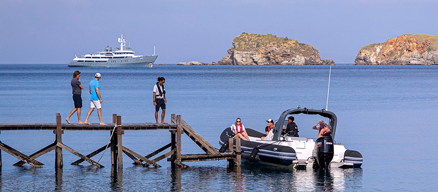 Travellers board a sleek tender from a wooden jetty as Aqua Blu anchors in calm blue waters beyond.
