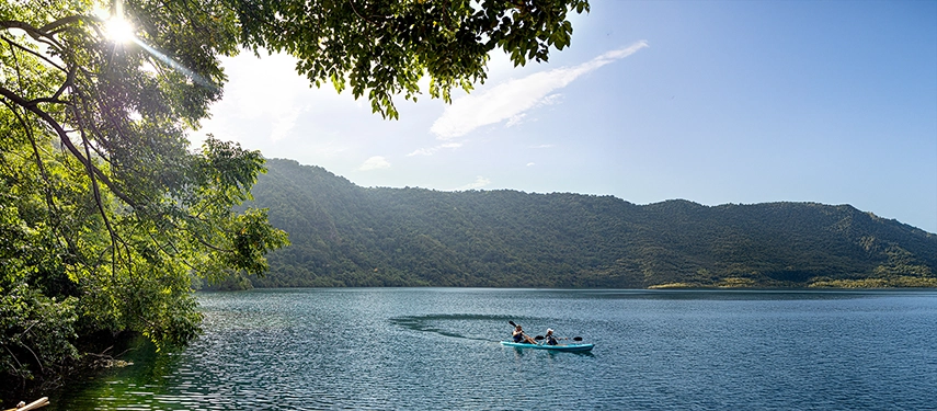 Kayakers glide across a still blue bay bordered by verdant hills, immersed in Indonesia’s wild coastal beauty.