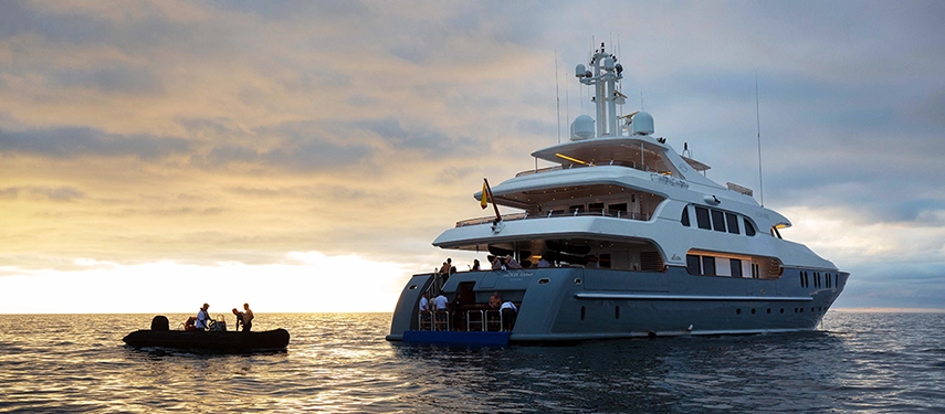 A Zodiac tender returns to Aqua Mare at sunset, the super-yacht glowing beneath a painted Galápagos sky.