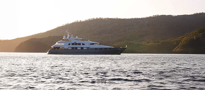 Aqua Mare floats peacefully before forested hills of the Galápagos, bathed in the warm, golden glow of late afternoon.