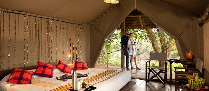 Couple enjoying a scenic view from a luxury tented suite at Basecamp Masai Mara, with Maasai beadwork decor enhancing the interior.