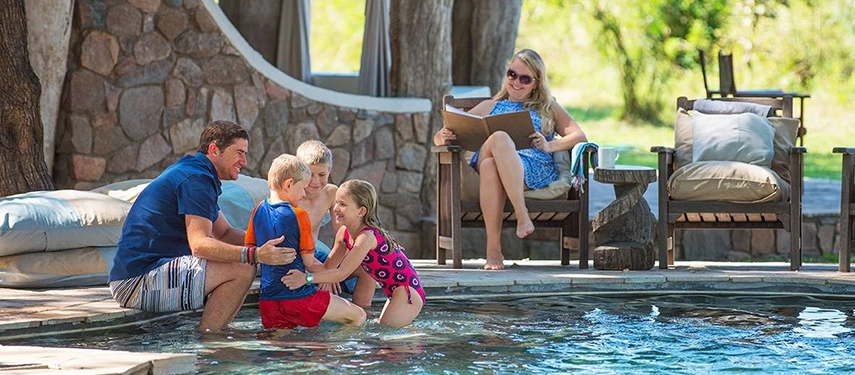 Father playing with three young children in a pool while a mother relaxes nearby during a family-friendly Grand Zambezi Safari.