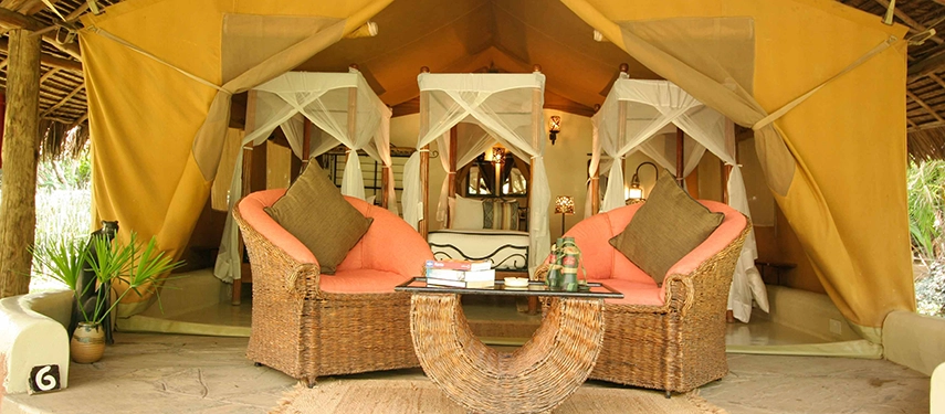 Open-front luxury safari tent at Basecamp Masai Mara, featuring twin canopy beds, wicker seating, and earthy décor for a comfortable stay in the wilderness.