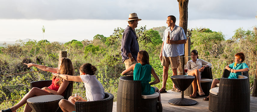 Family on the balcony of Galápagos Safari Camp enjoying drinks and a snack while looking across the forest and out to sea