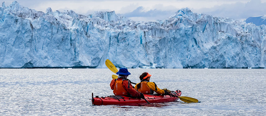 Two kayakers paddling towards a glacier on an the Arctic – Aurora Expeditions adventure.
