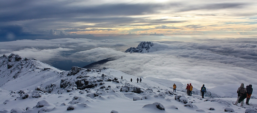 Trekkers making their descent through snow-covered slopes on Kilimanjaro under dramatic cloud-filled skies.