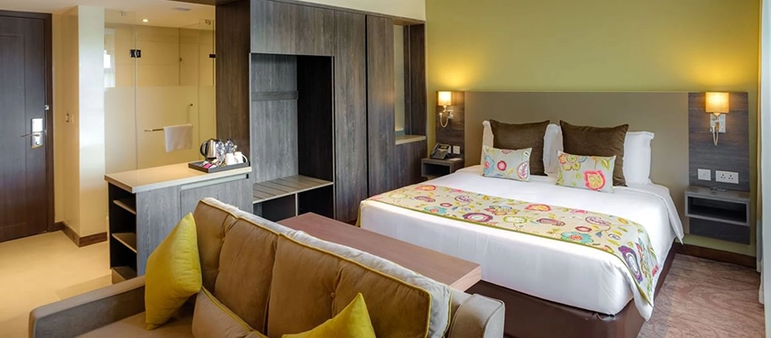 Modern hotel executive suite with king bed, sofa, open wardrobe, and ensuite bathroom, blending contemporary style with comfort.