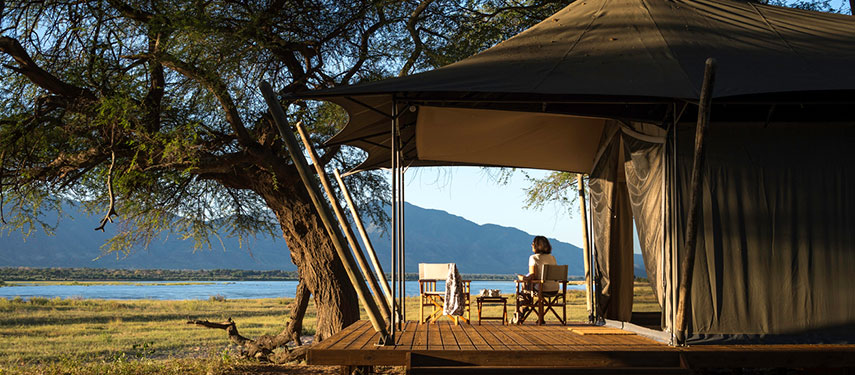 Female guest searches for game from her tented suite at Ruckomechi safari camp in Mana Pools National Park, Zimbabwe