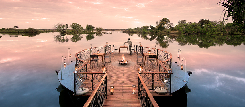 Romantic wooden deck with firepit extending over the river, surrounded by lanterns and pink skies.