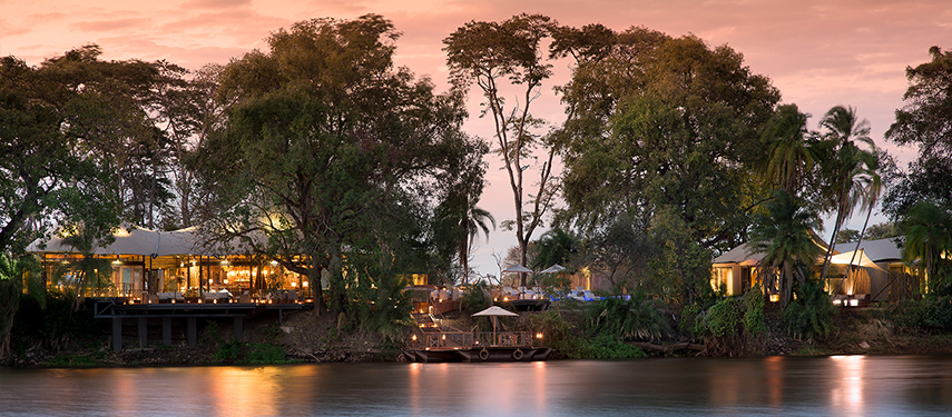 Twilight view of the luxurious Thorntree River Lodge nestled among trees on the banks of a calm river.