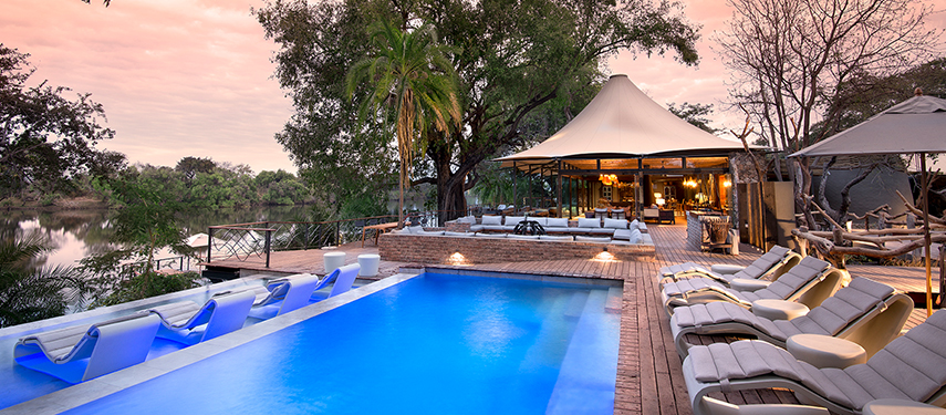 Thorntree River Lodge pool area at sunset, with sun loungers, palm trees, and open-air tented lounge.