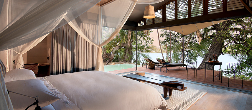 Elegant en suite safari tent with canopy bed, private plunge pool, and river views through open walls.