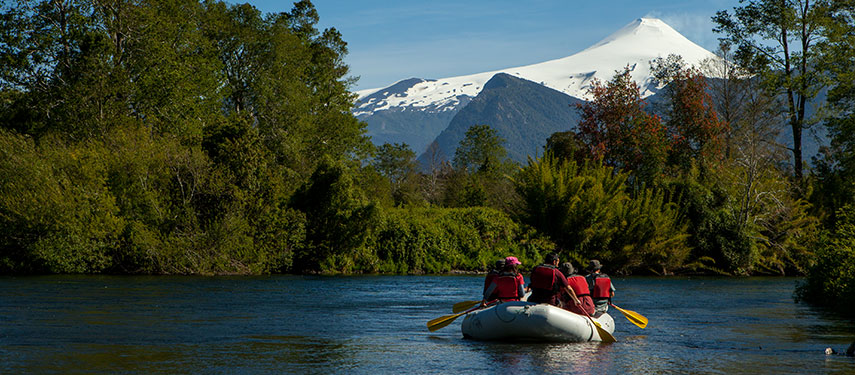 Group of tourists rafting on Liucura River in Chile's Lake District with snowcapped mountains in the background
